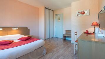 Una habitación de hotel con cama, mesita de noche, silla, escritorio, lámpara y una puerta que da a otra habitación.