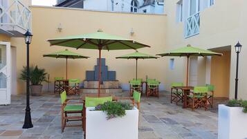 Un patio al aire libre con varias mesas y sillas, sombrillas verdes y plantas en macetas.