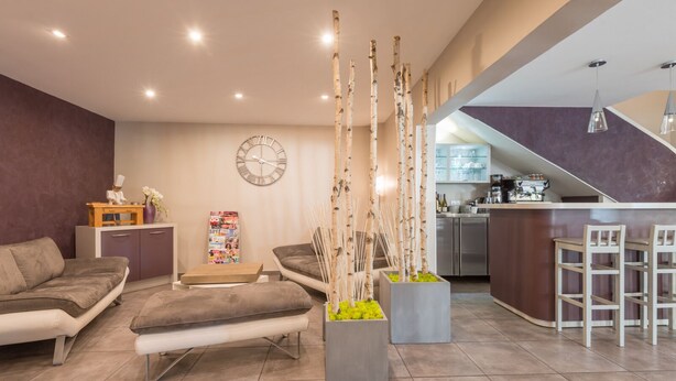 A modern living room with a sofa, a coffee table, and decorative plants. There is a kitchen area with a bar and seating. - Le Réverbère - La Cuisinerie - L'Hôtellerie (Vic-en-Bigorre)