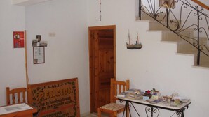 Une pièce comprenant un bureau en bois, une chaise, une petite table sur laquelle se trouvent divers objets, un escalier avec une rampe en fer forgé et une porte donnant sur une autre pièce.