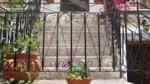 Un bâtiment à deux étages, doté d’une façade en pierre, d’un balcon avec des balustrades en métal et d’un escalier menant à l’étage supérieur.