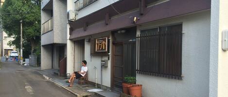 A building with a sign that reads "Guest House" and a person sitting on a bench outside.