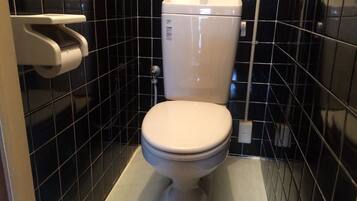 Een toilet in een badkamer met zwart betegelde muren en een witte toiletbril.