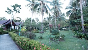 Un jardin tropical agrémenté de palmiers, un sentier et une structure traditionnelle en bois.