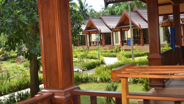 Une construction traditionnelle en bois, dotée de nombreuses pièces, entourée d’une végétation luxuriante et d’un jardin bien entretenu.