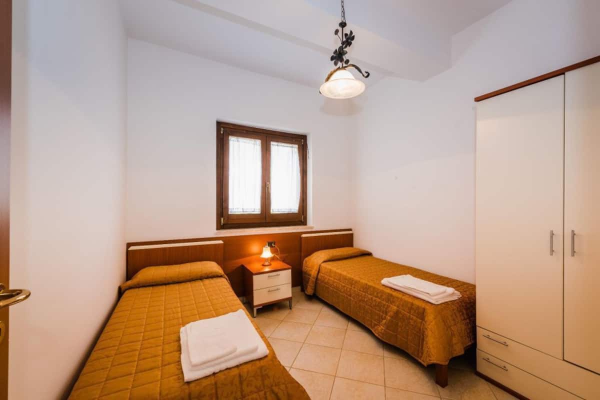 Une chambre avec deux lits, une table de chevet, une armoire et une fenêtre avec des rideaux.