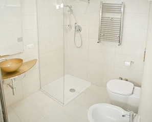 A modern bathroom with a glass-enclosed shower, a white sink with a beige bowl, a toilet, and a bidet. - Let's Go To Rome (Rome)