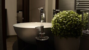 Ein modernes Badezimmer mit einem runden Waschbecken, einem Wasserhahn und einem Blumentopf.
