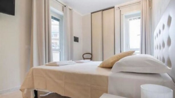 Ein Hotelzimmer mit einem Bett, einem Sessel, einem Nachttisch und einem Fenster mit Vorhängen.