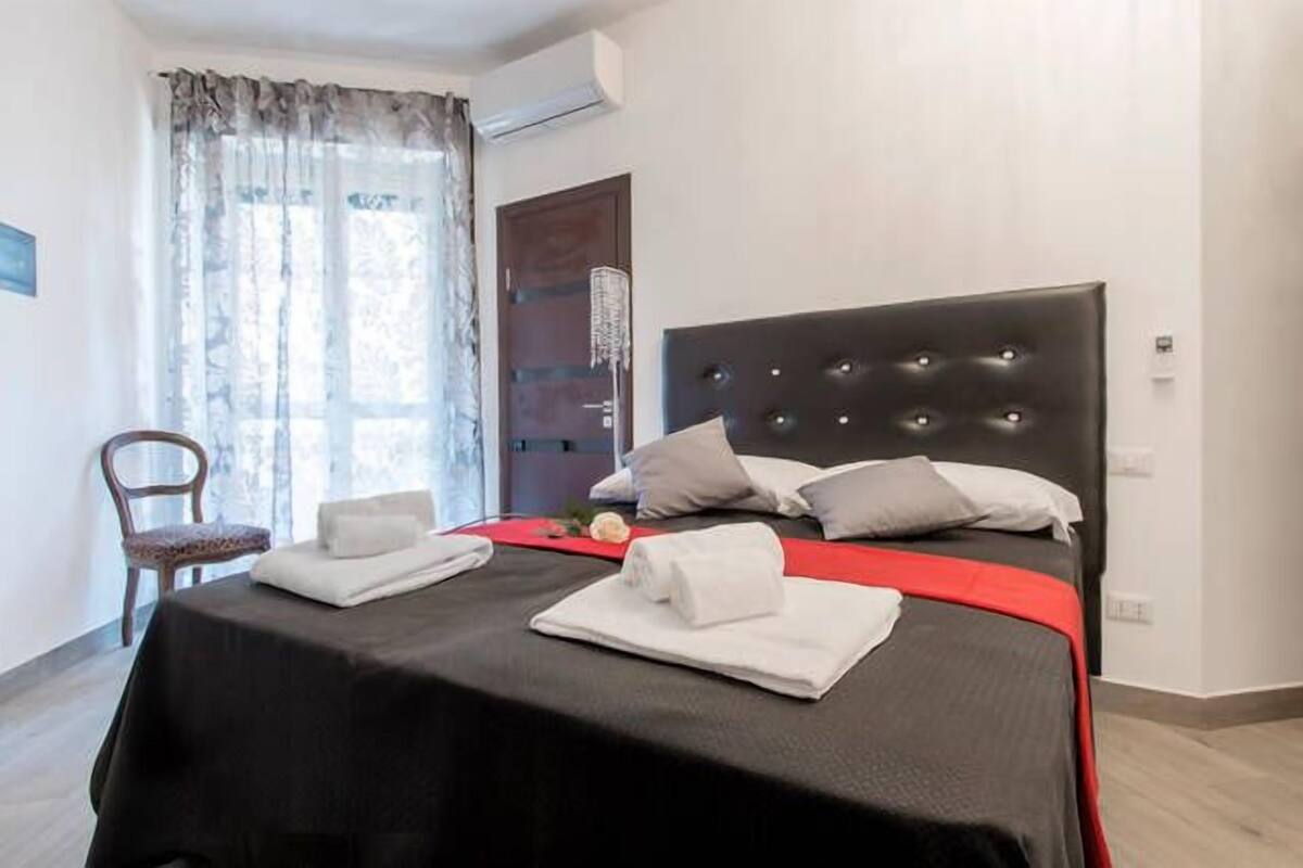 A hotel room with a large bed, a chair, and a window with curtains.