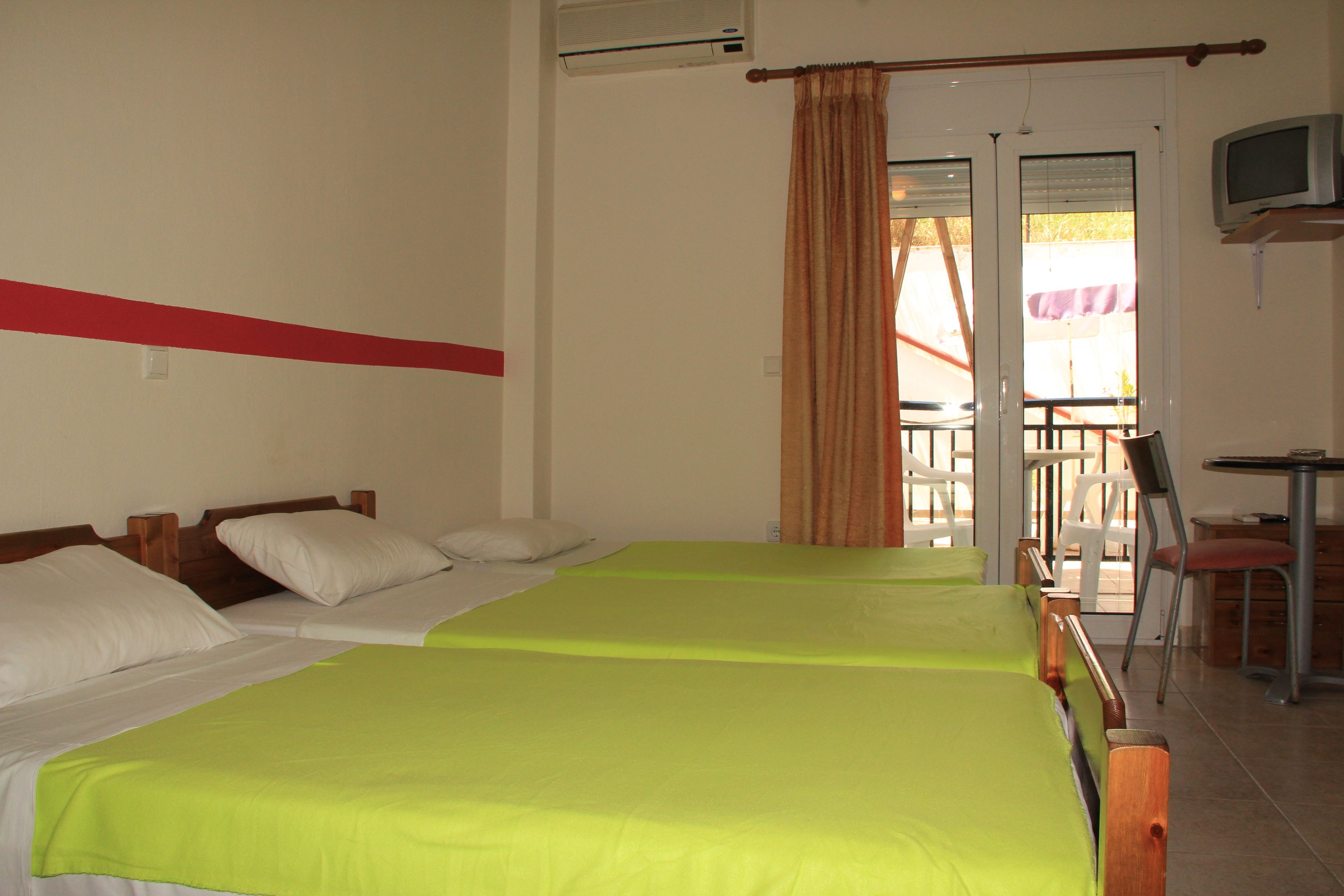 A hotel room with two beds, a TV, and a balcony with chairs.