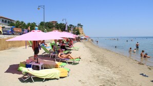 Une plage avec des transats et des parasols, un ciel dégagé et des gens dans l’eau.
