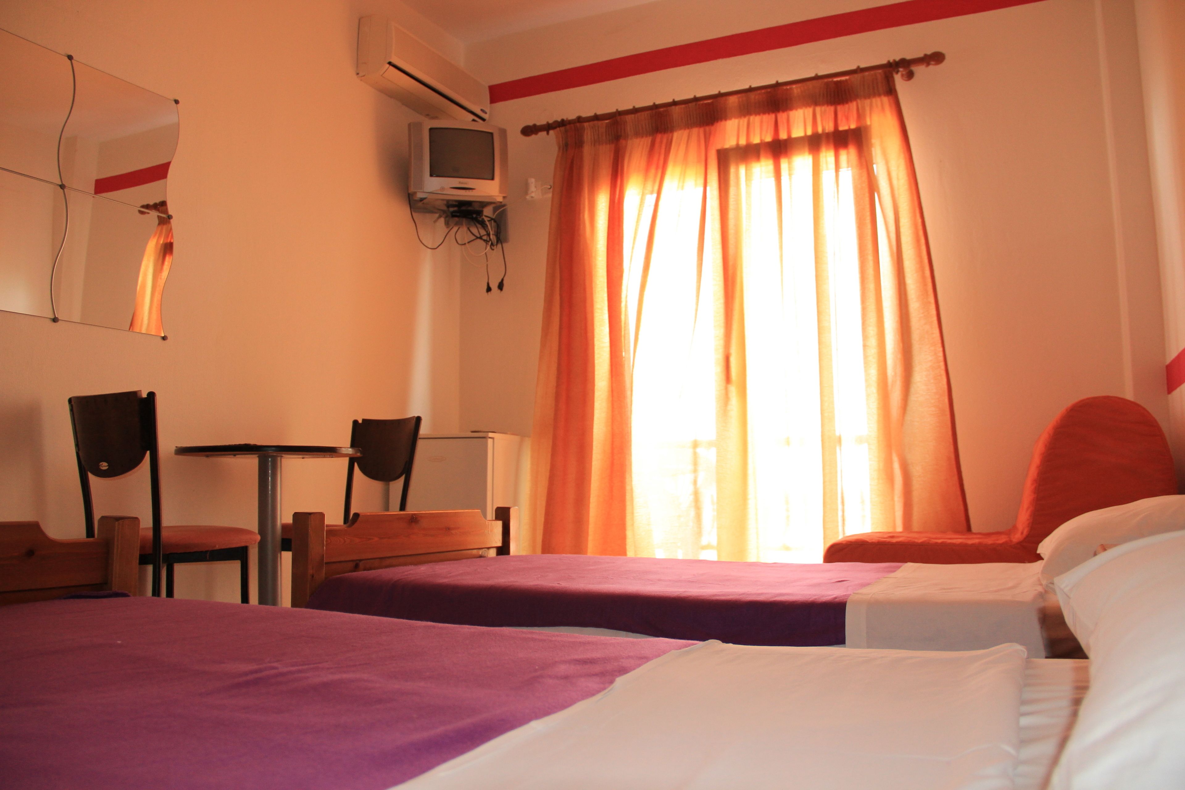 Una habitación de hotel con dos camas, un escritorio, sillas, un televisor y cortinas.