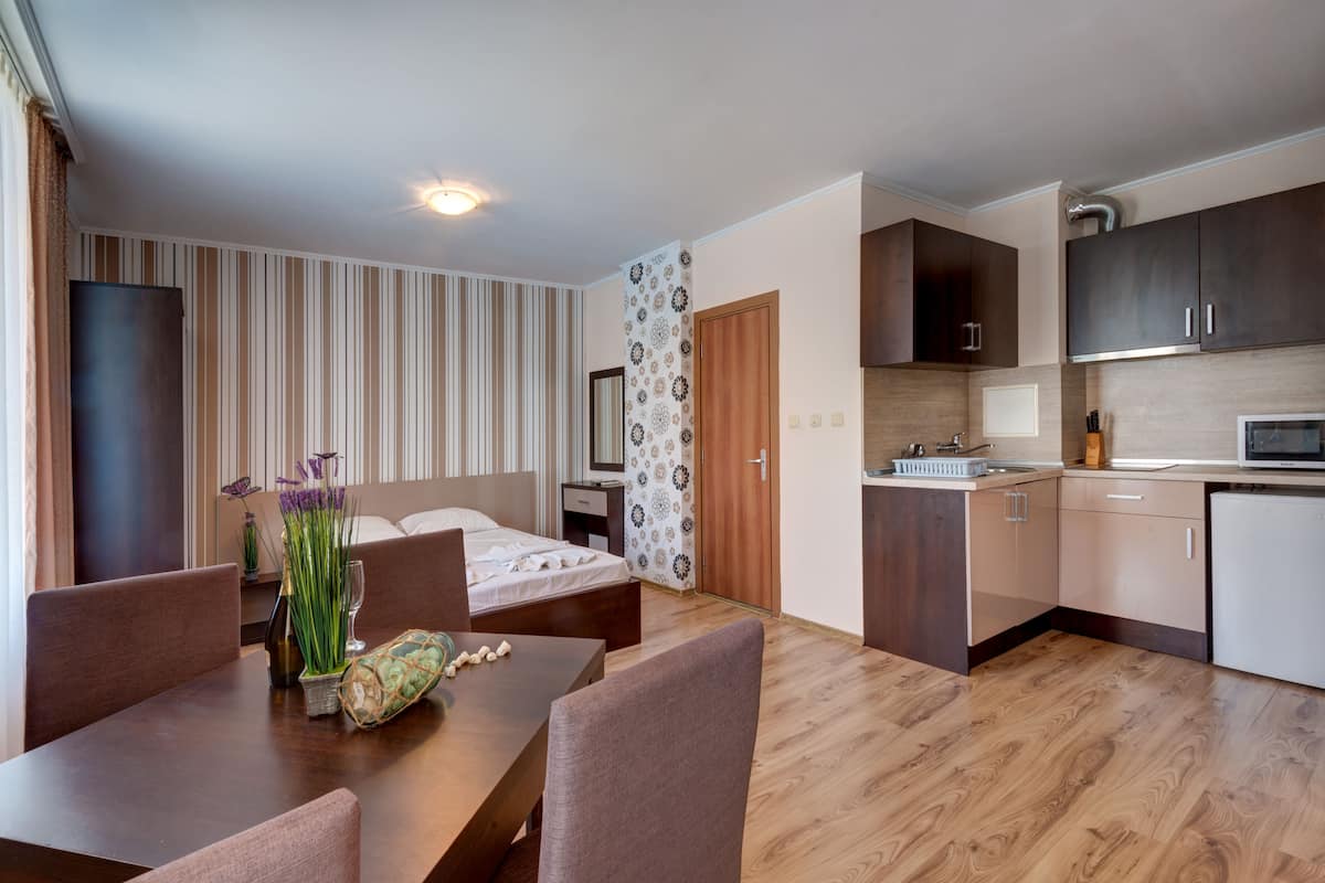 Ein modernes Hotelzimmer mit einem Holztisch, einem Bett mit Kopfteil, einer Küchenzeile mit Schränken und einer Mikrowelle sowie einer gestreiften Wand.