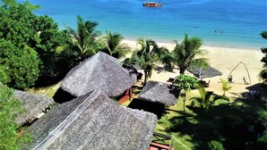 Een strand met rieten hutten, palmbomen en een boot op het water.