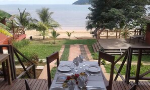 A dining table set for two with a view of the beach and ocean. - Madagascar Resort Ambaro Beach (Nosy Be)