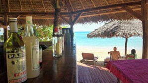 Een strandbar met drankflessen, een houten tafel en uitzicht op het strand en de oceaan.