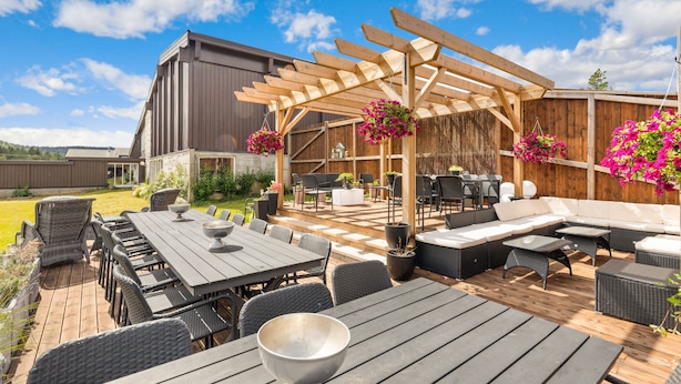 A covered outdoor patio with a wooden pergola, wicker furniture, and hanging flower baskets.