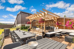 A covered outdoor patio with a wooden pergola, wicker furniture, and hanging flower baskets.
