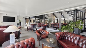A spacious lobby with leather sofas, a flat-screen TV, and a staircase leading to upper floors.