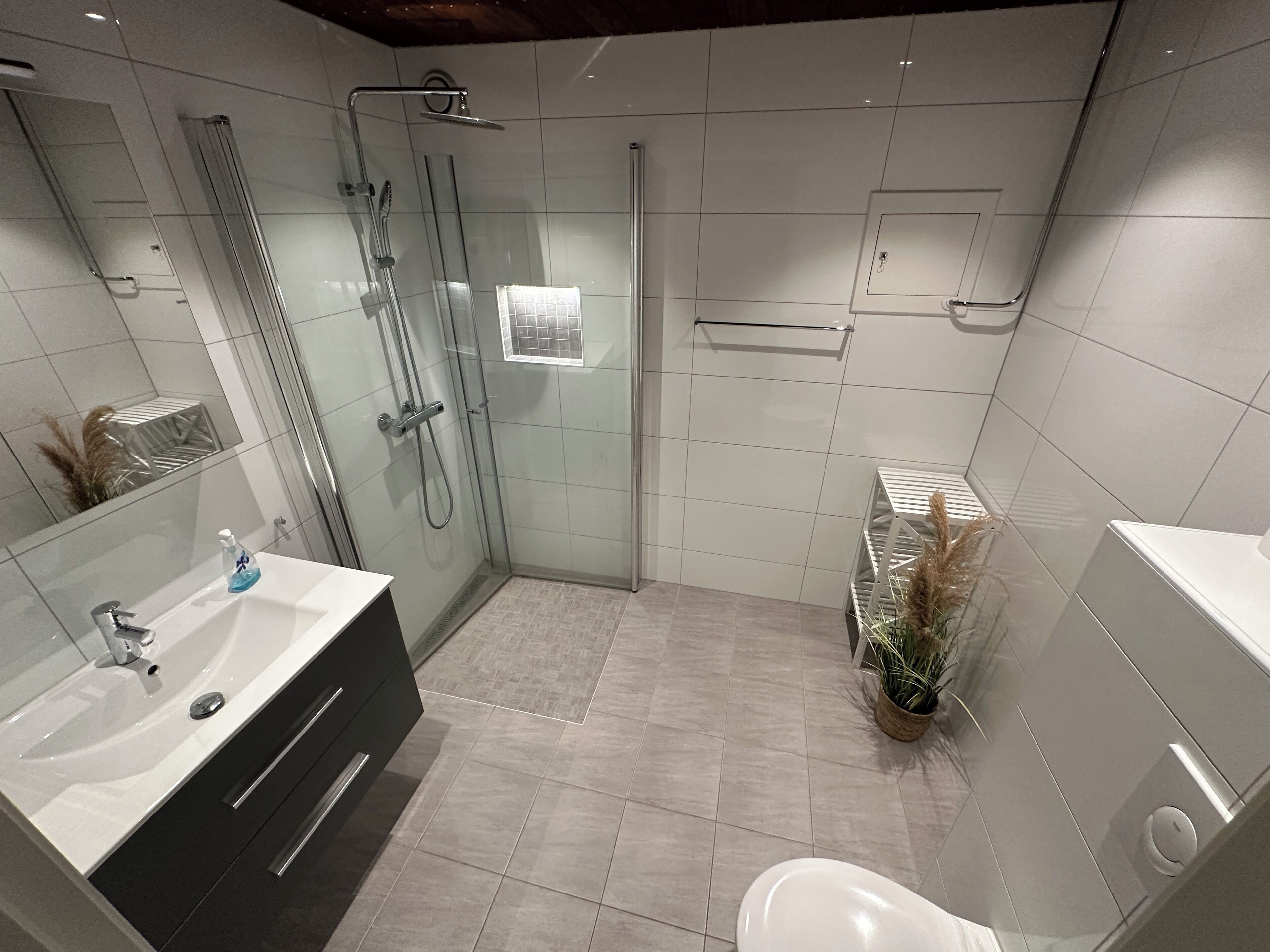 A modern bathroom with a glass-enclosed shower, a white sink with a dark cabinet, and a toilet.