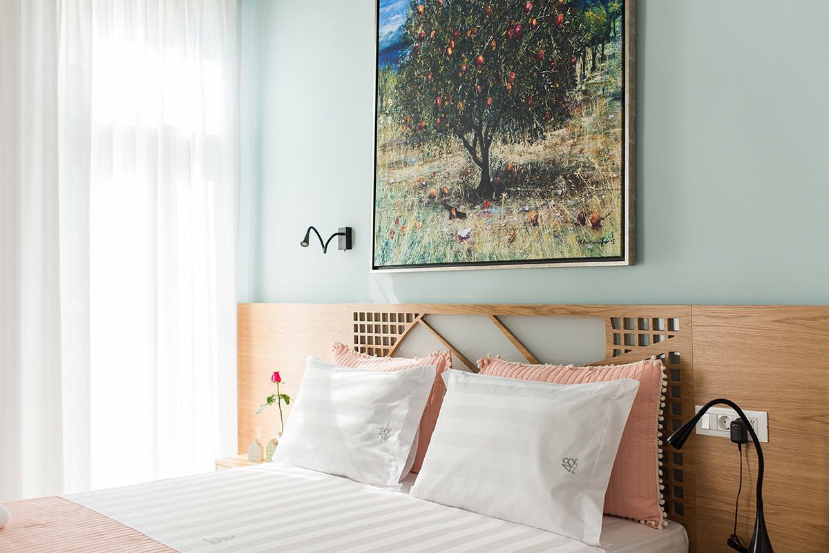 Una cama bien tendida con ropa de cama blanca y rosa, un cabecero de madera y un cuadro de un árbol colgado en la pared.