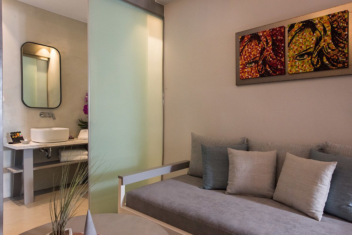 Een moderne badkamer met een grijze bank, een grote spiegel en een kunstwerk aan de muur.
