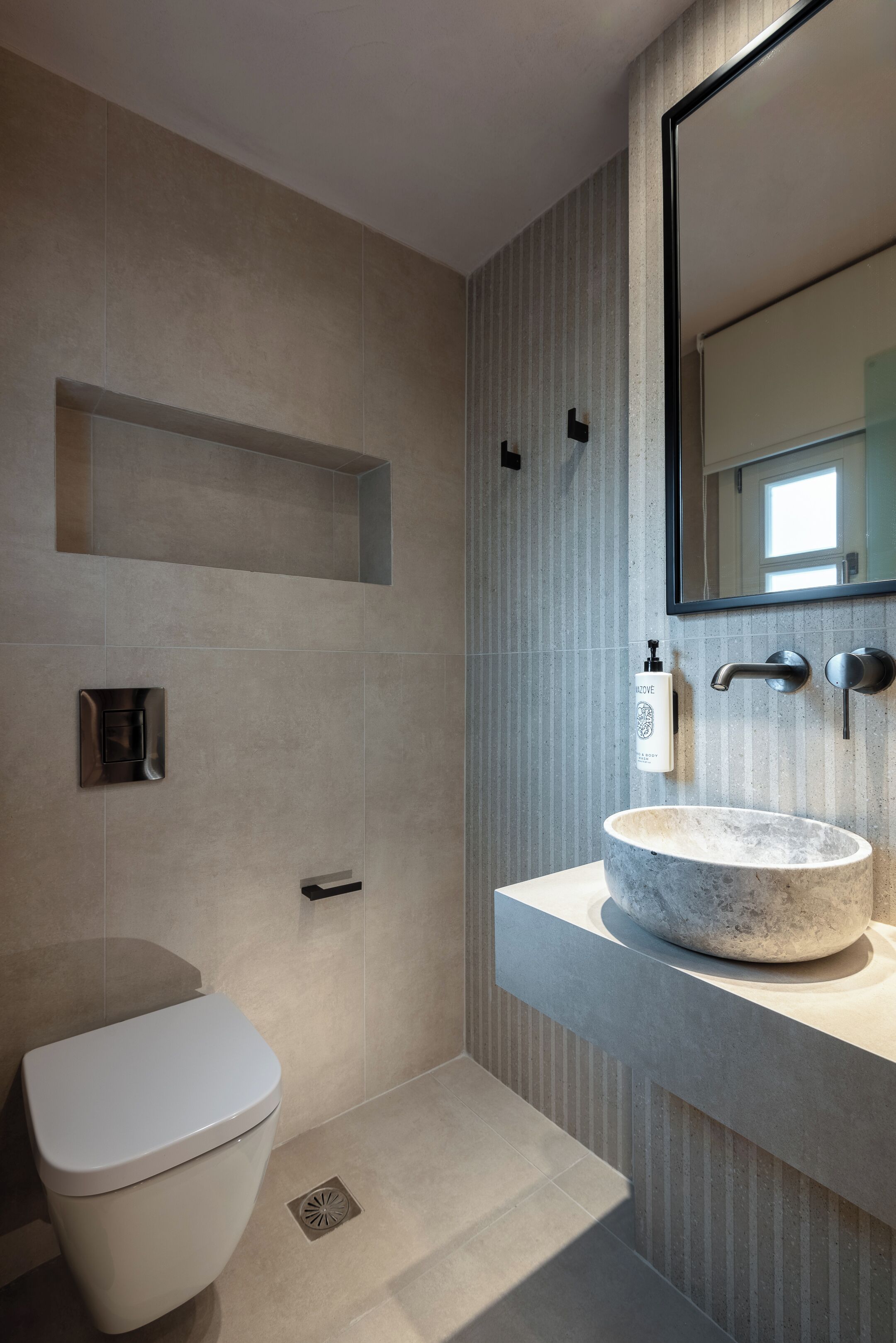A modern bathroom with a white toilet, a large marble sink, and a wall-mounted mirror.