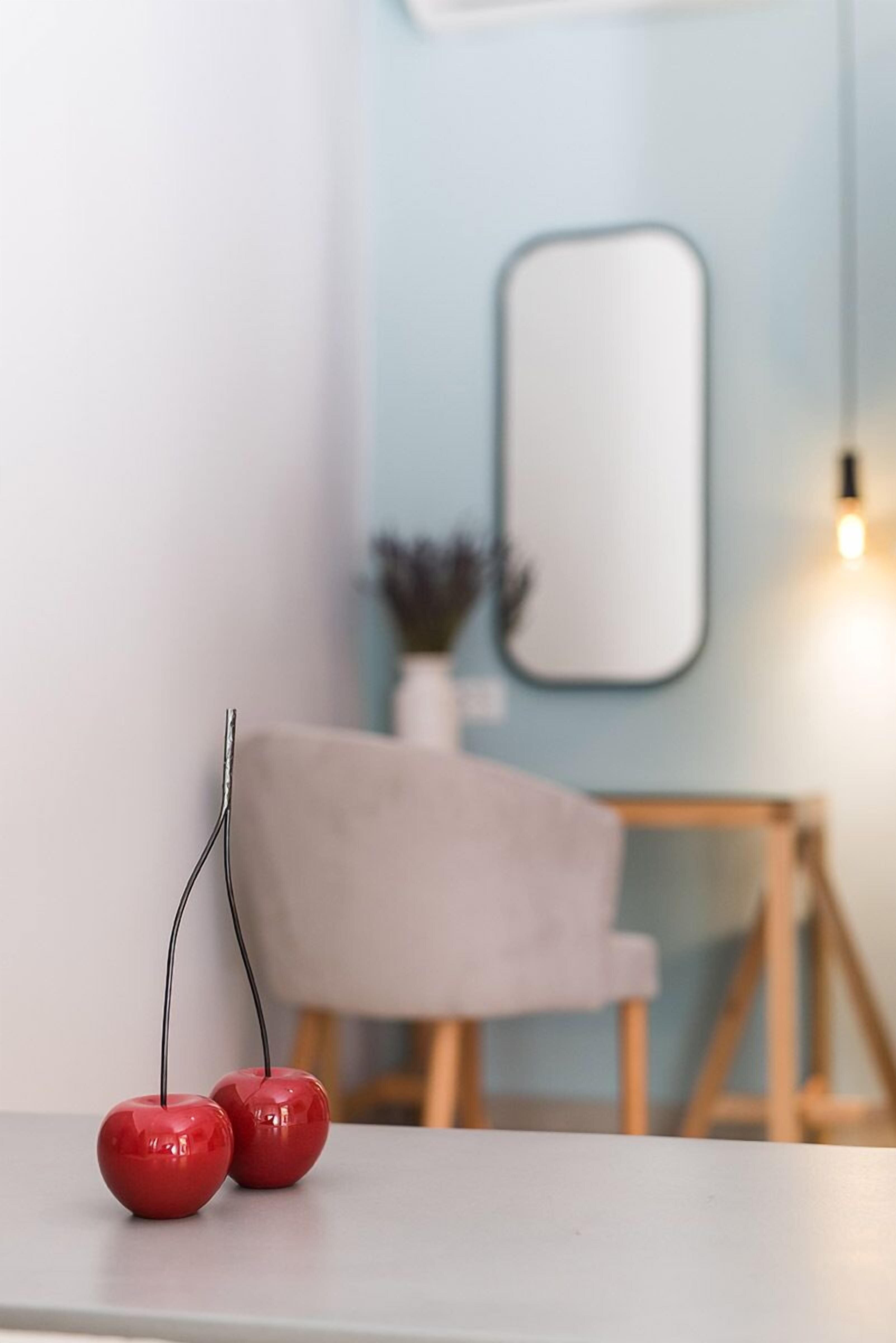 A minimalist room with a grey sofa, a small table with two red spherical objects, and a wall-mounted mirror.