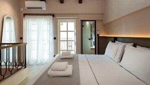 Habitación de hotel con una cama grande, cabecero de madera, balcón con barandilla y puerta que da a un baño.
