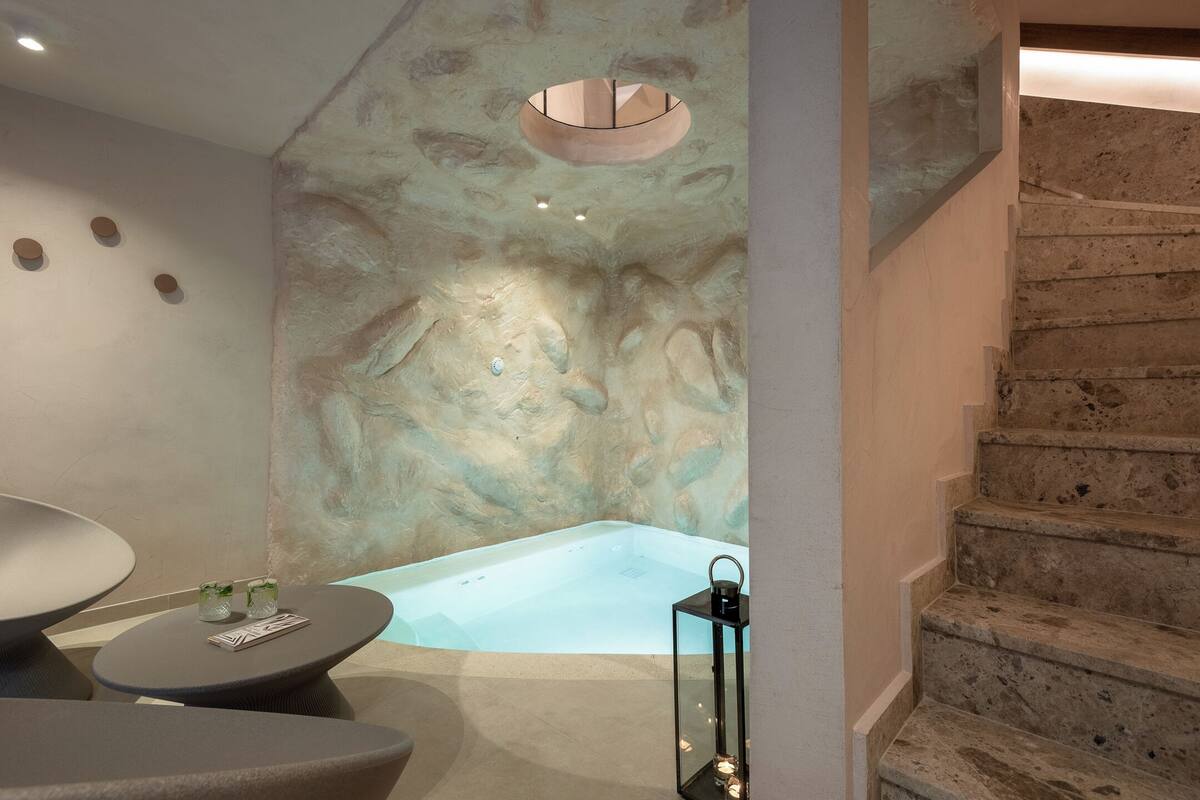 Un área de spa con una bañera grande, una mesita con un libro y un farol.