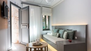 Una habitación de hotel moderna con sofá cama, una mesita redonda con velas, televisor de pantalla plana en la pared y un ventanal con vistas al exterior.