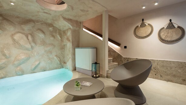 Un área de spa moderna con una pared de piedra, una bañera, un espacio para sentarse y una escalera.