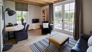 Una sala de estar moderna con techo de madera, una mesa de comedor con sillas, un sofá, un televisor y vistas al exterior a través de amplios ventanales.