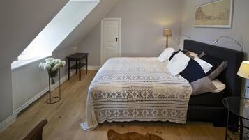 Une chambre avec un puits de lumière, un lit recouvert d’une couvre-lit à motifs, une table de chevet, une lampe et un tableau encadré accroché au mur.