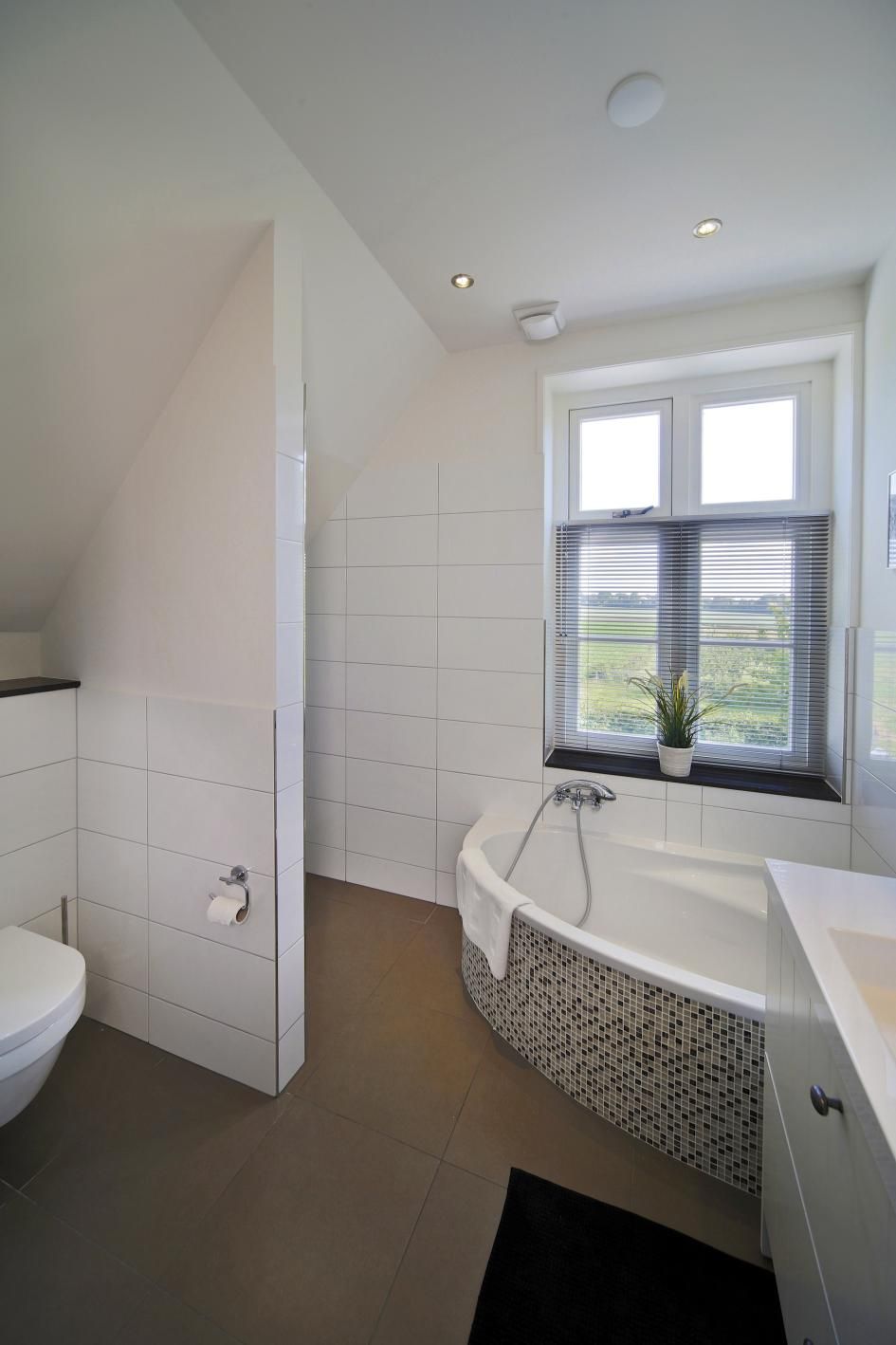A modern bathroom with a freestanding bathtub, a toilet, and a window with blinds.