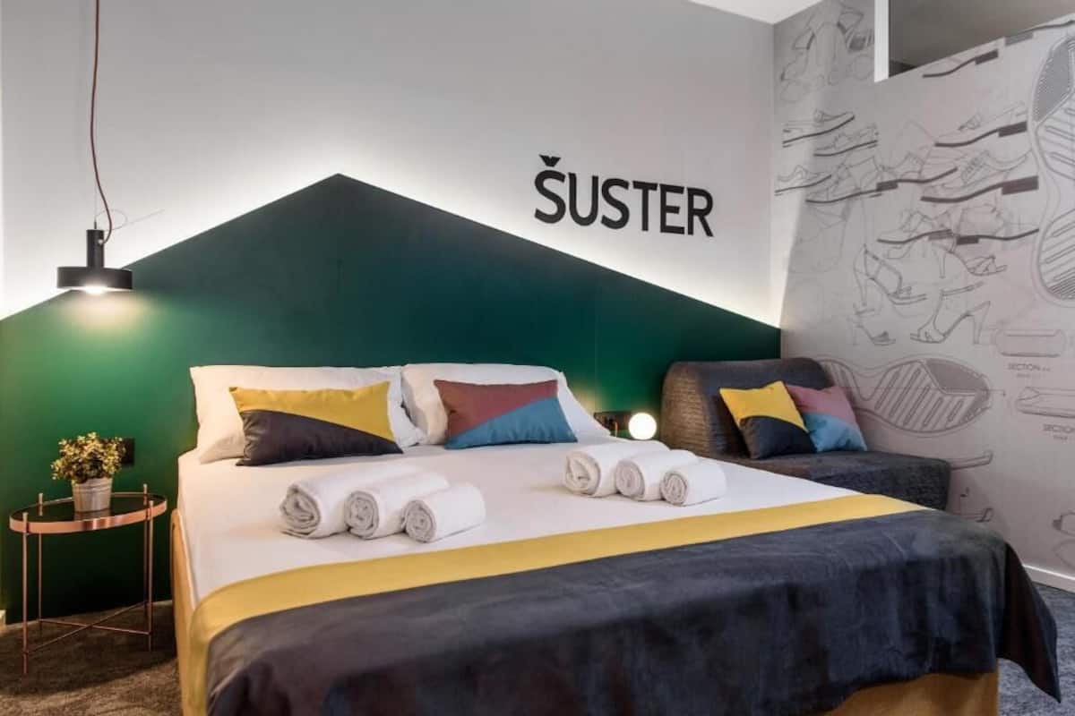 Ein modernes Hotelzimmer mit Bett, Kissen, einem Nachttisch mit Pflanze und einer Wand mit Schuhmotiv.