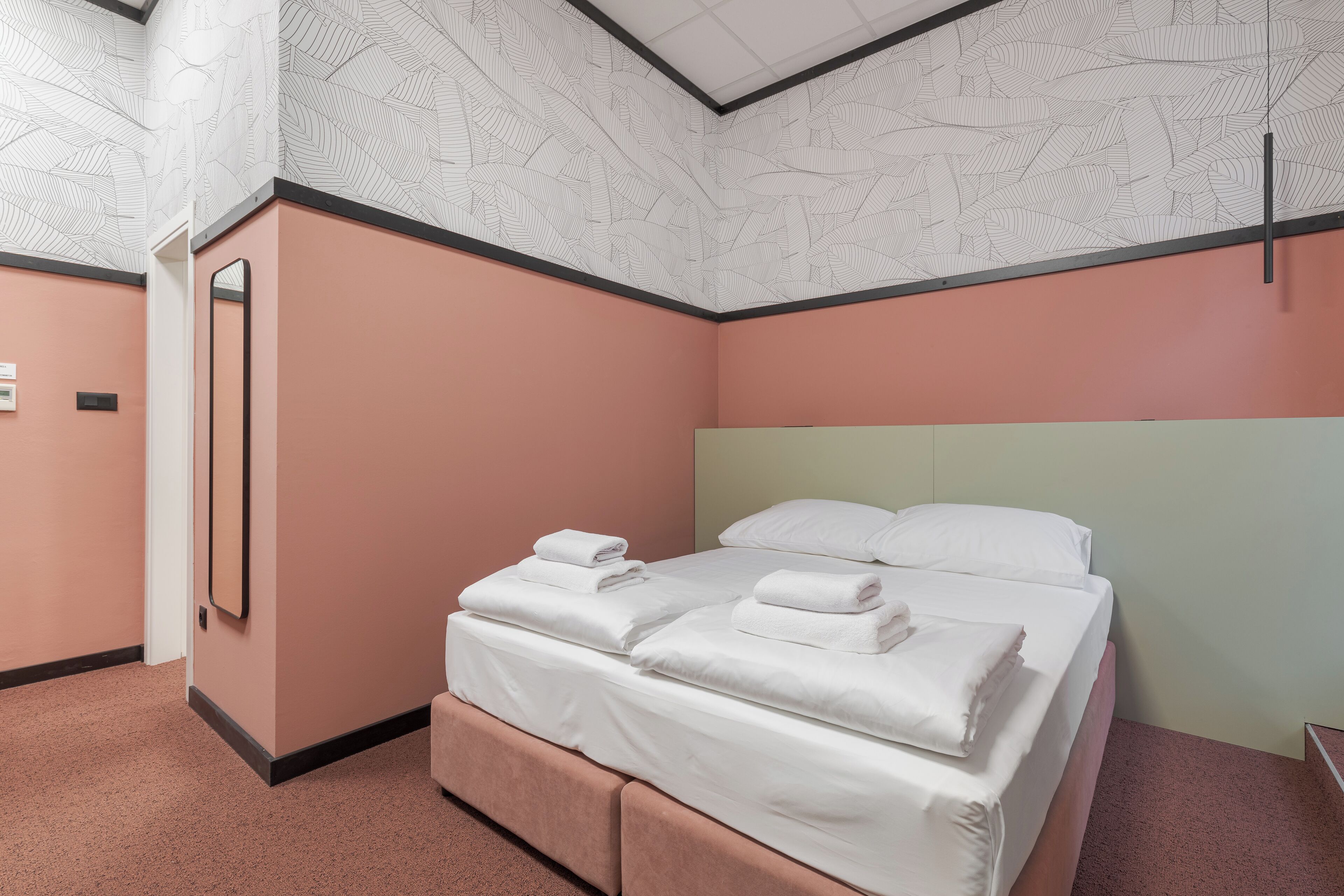 Ein ordentlich bezogenes Bett mit weißen Leinen und Kissen, ein Spiegel an der Wand und eine gemusterte Decke.