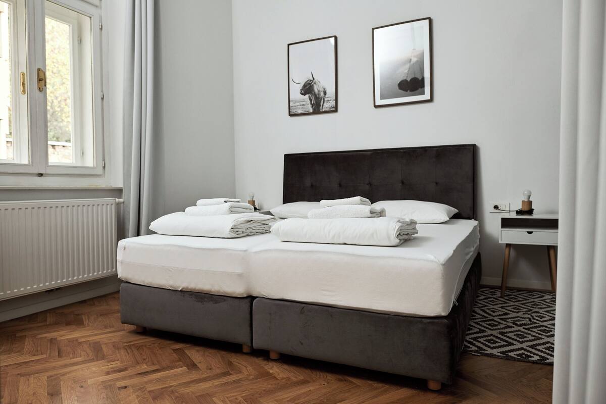 Ein Schlafzimmer mit einem Bett, zwei gerahmten Bildern, einem Nachttisch und einem Heizkörper.