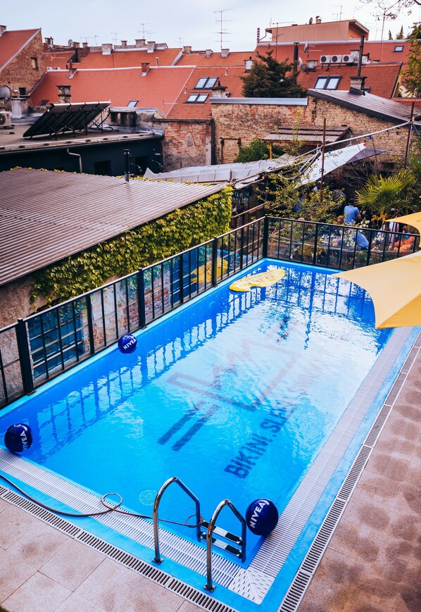 A rooftop swimming pool with clear blue water, surrounded by a metal fence and a yellow canopy. - Stay Swanky (Zagreb)