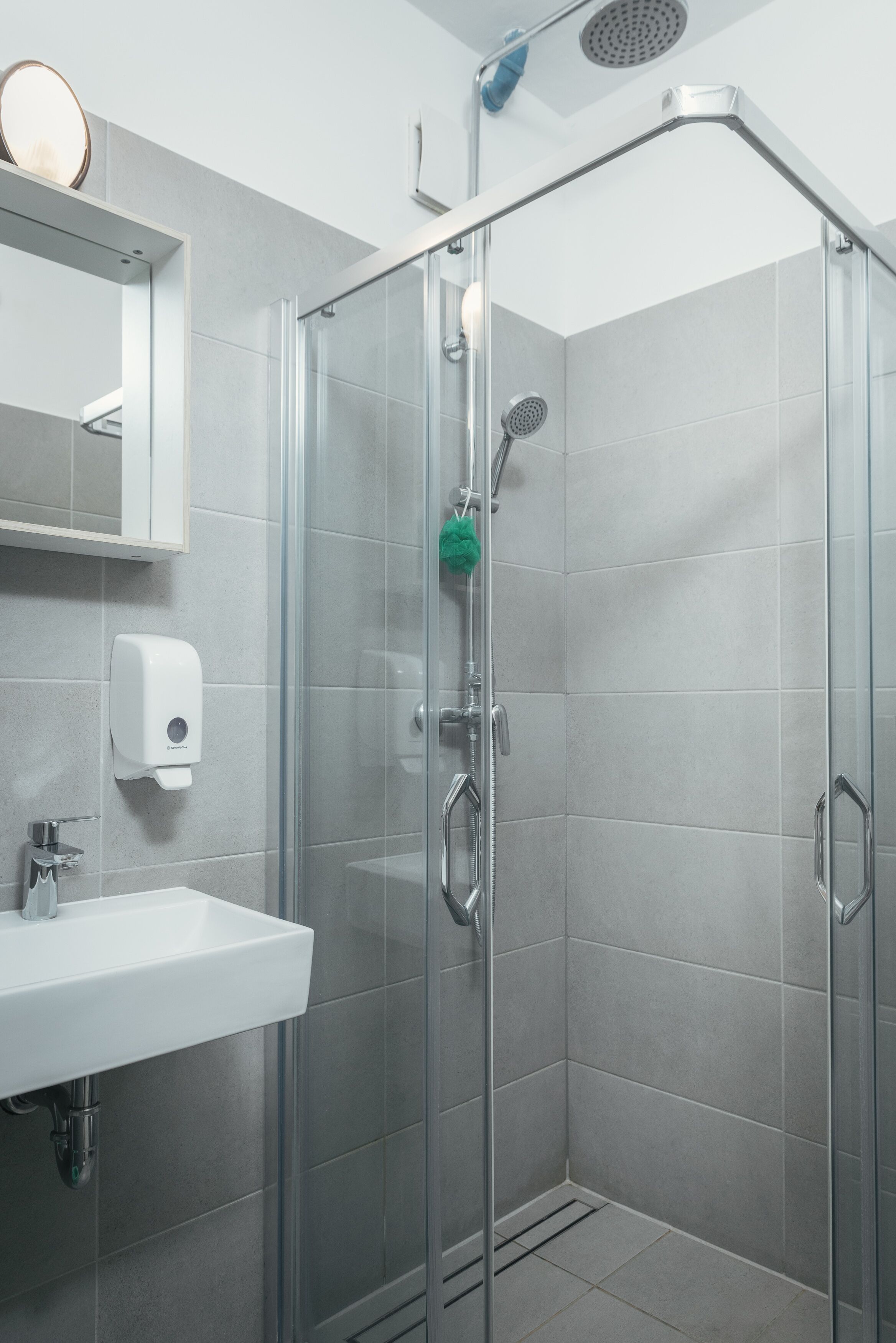 A modern bathroom with a glass-enclosed shower, a white sink, and a soap dispenser.