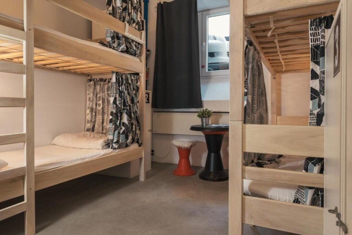 A bunk bed room with a window, a small table, and a plant.