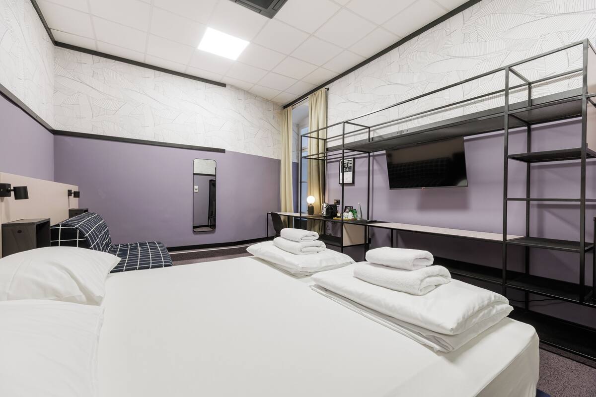 Ein Hotelzimmer mit einem Bett, einem Schreibtisch, einem Stuhl, einem Fernseher und einem Etagenbett.