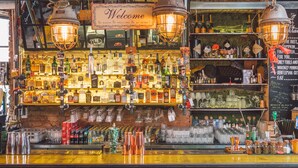 Un bar con un letrero que dice 'Welcome', diversas botellas de licor y faroles colgantes.