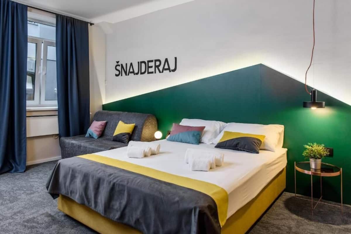 Ein Hotelzimmer mit einem Bett, einem Sofa, einem kleinen Tisch mit Pflanze und einem Fenster mit Vorhängen.