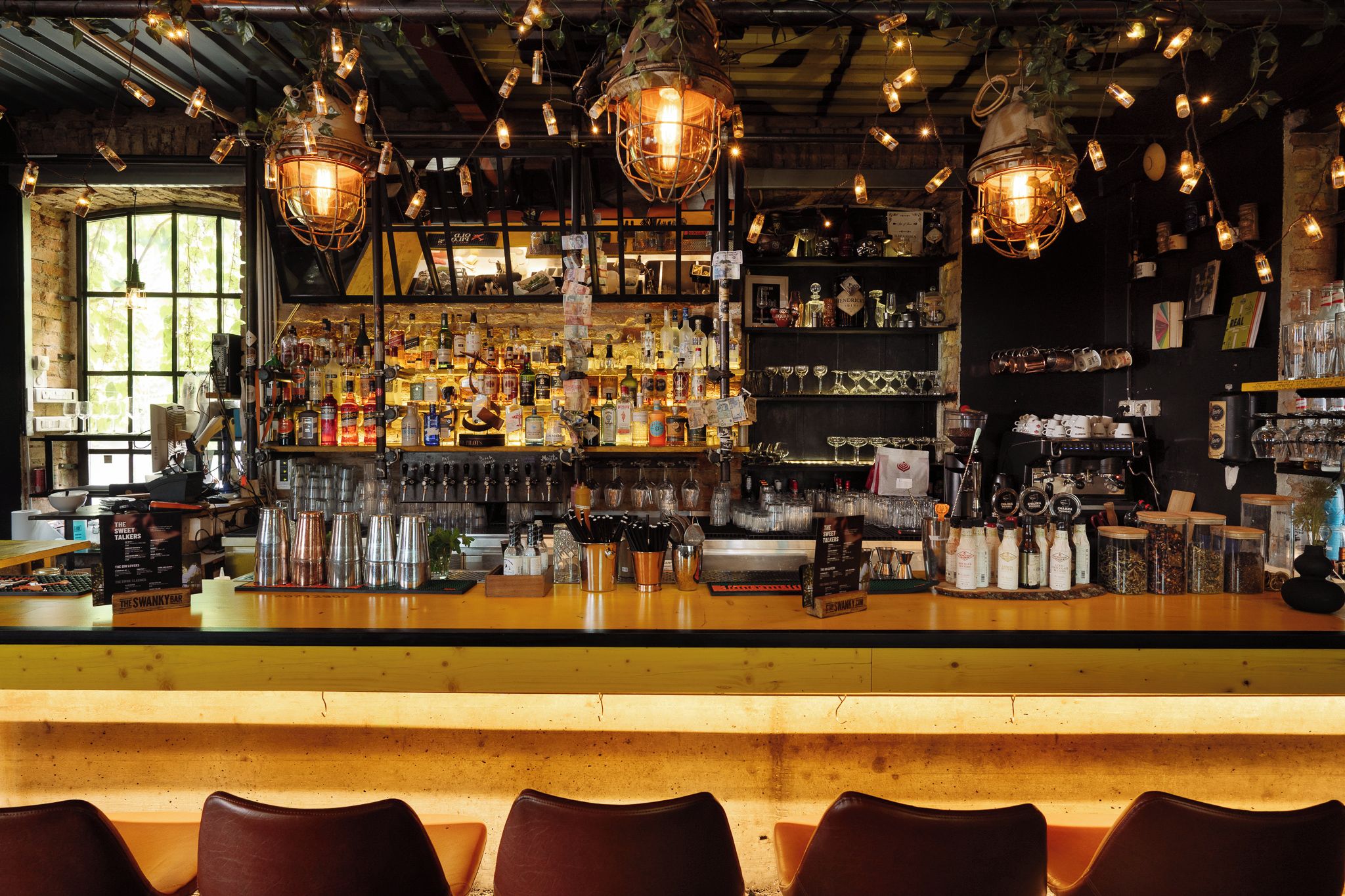 A bar with a wooden counter, multiple bottles, glasses, and a variety of bar tools.