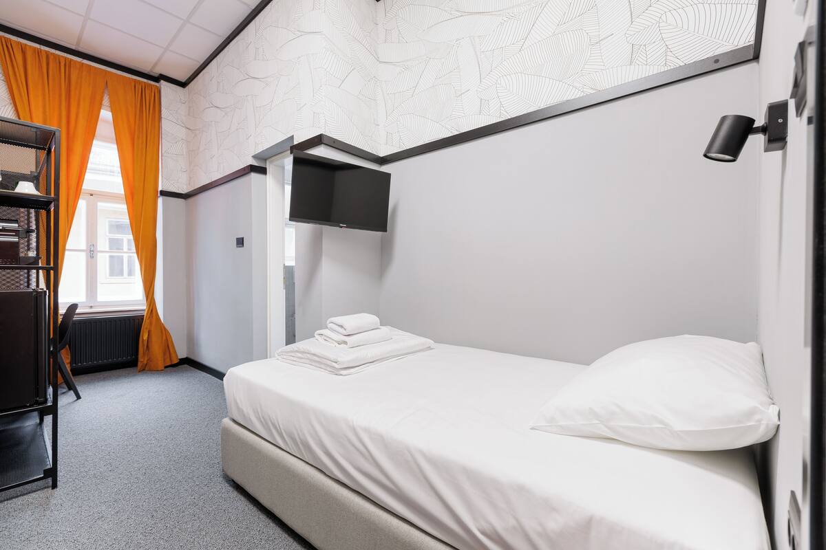 Ein ordentlich eingerichtetes Hotelzimmer mit einem Bett, einem Schreibtisch und einem an der Wand befestigten Fernseher.