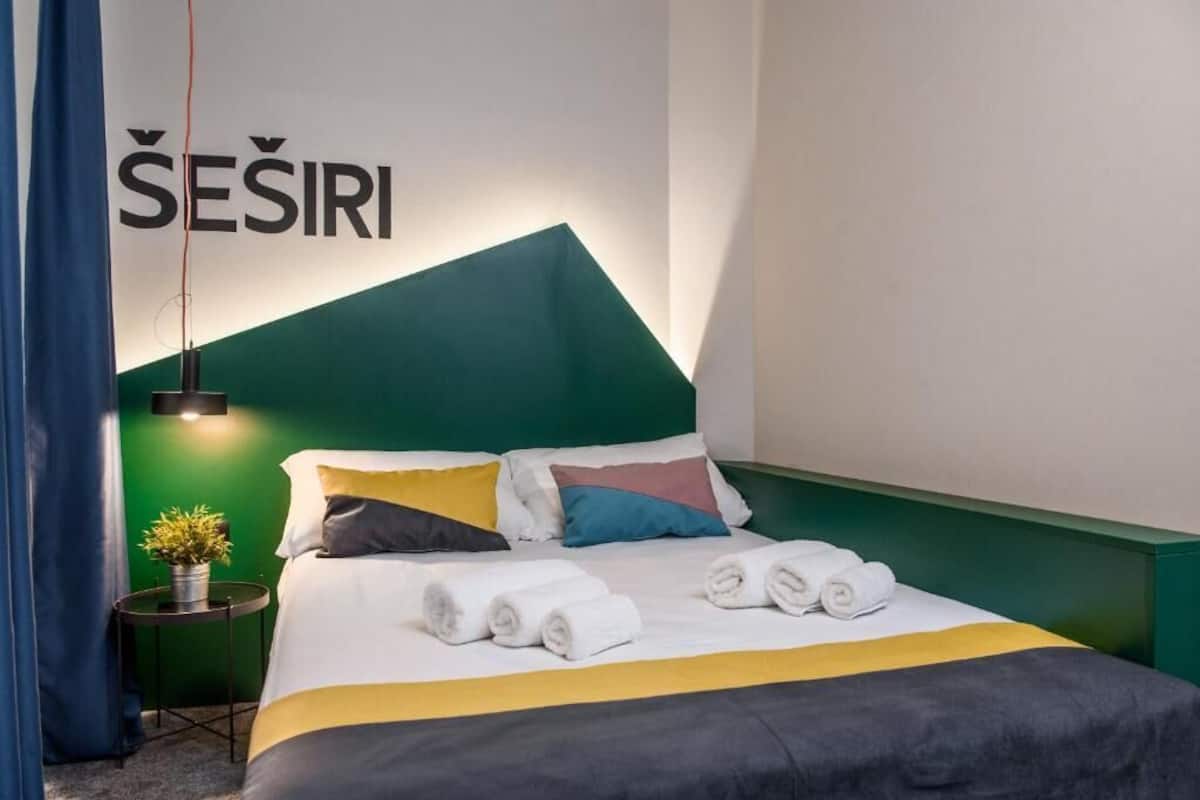 Ein Hotelzimmer mit einem grünen Kopfteil, einem Bett mit weißer und gelber Bettwäsche und einem an der Wand befestigten Schild mit der Aufschrift 'SEŞIRI'.