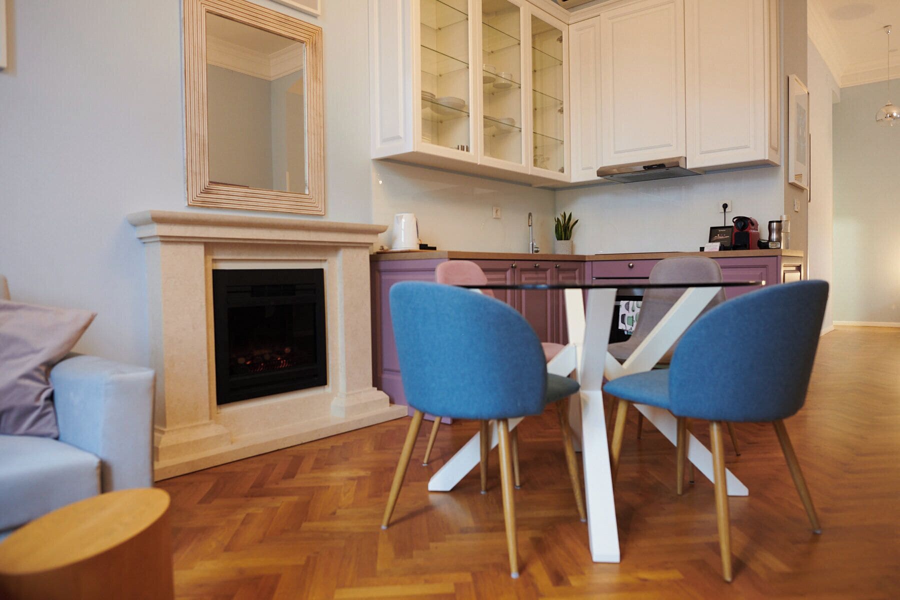 Una cocina moderna con armarios blancos, una mesa de comedor con cubierta de vidrio y dos sillas azules.
