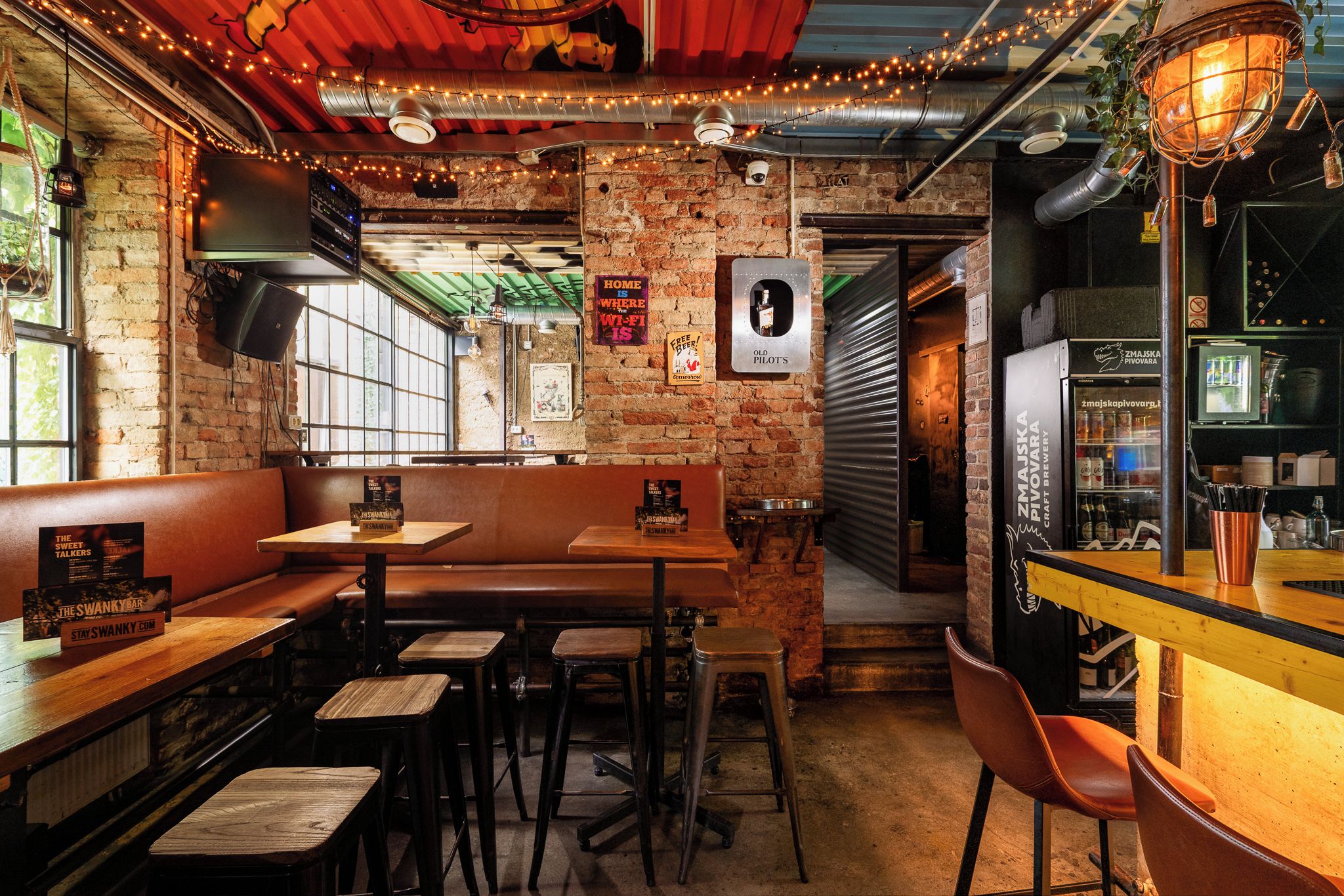 A cozy bar with brick walls, wooden furniture, and string lights.